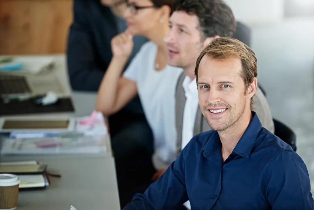 homme qui sourit à une table avec d'autres salariés